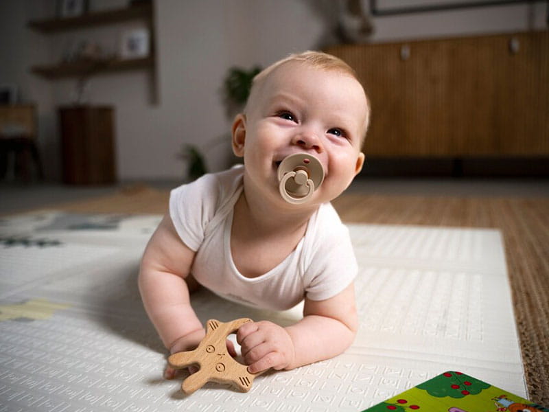 Bebê com chupeta e roupas claras brincando no chão e engatinhando