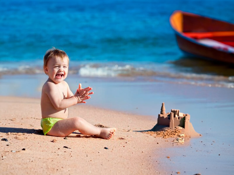Criança na praia com castelinho de areia