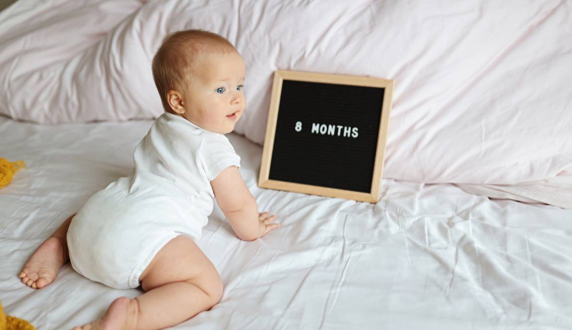 Bebê de 8 meses em cama com letreiro