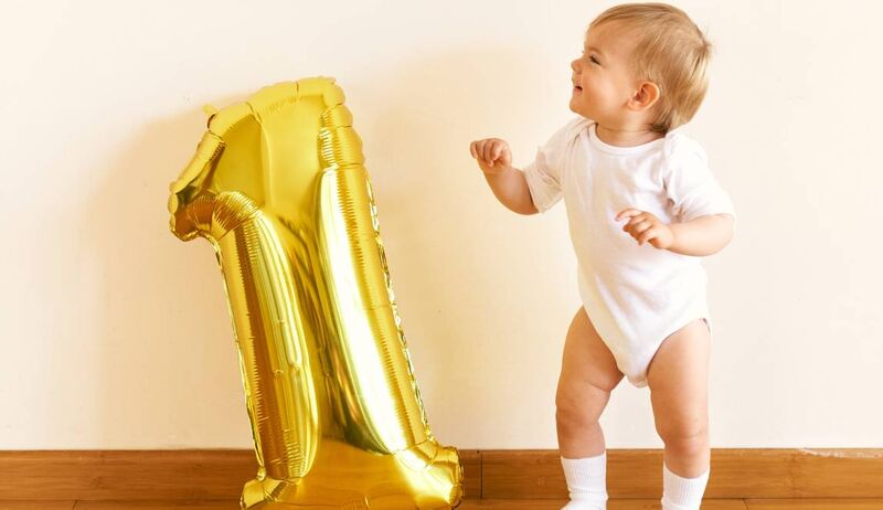 Bebê sorridente ao lado de balão dourado número um