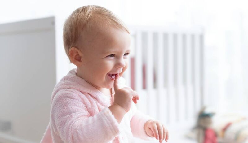 Bebê sorridente com dedo na boca em ambiente claro