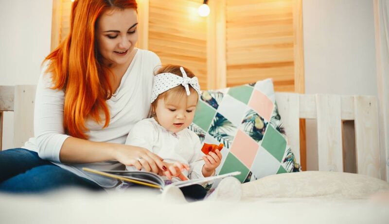 Mãe lendo livro para a filha na cama