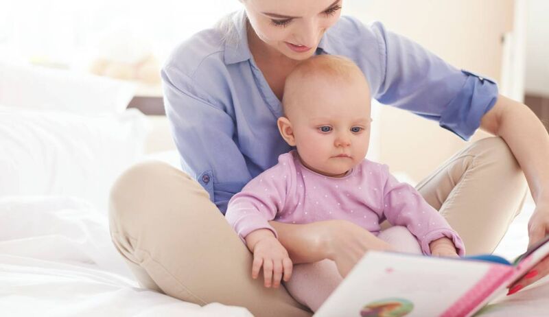 Mãe lendo livro para bebê em quarto decorado.