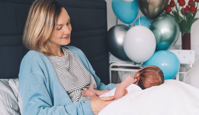 Mãe segurando bebê em ambiente festivo com balões