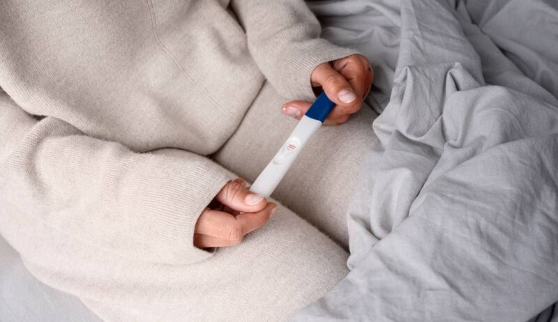 Mulher segurando teste de gravidez em cama