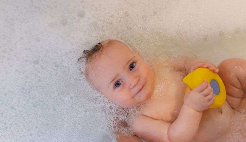 Bebê sorridente brincando na banheira com espuma