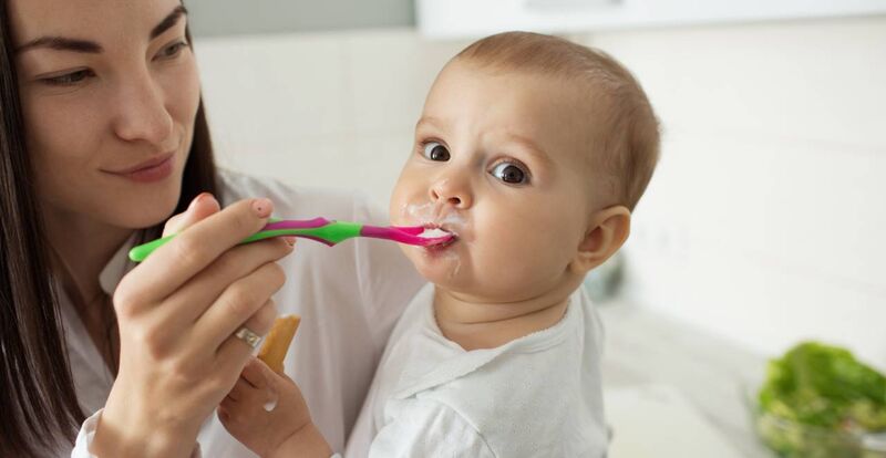 Mãe escovando os dentes de um bebê feliz na cozinha.